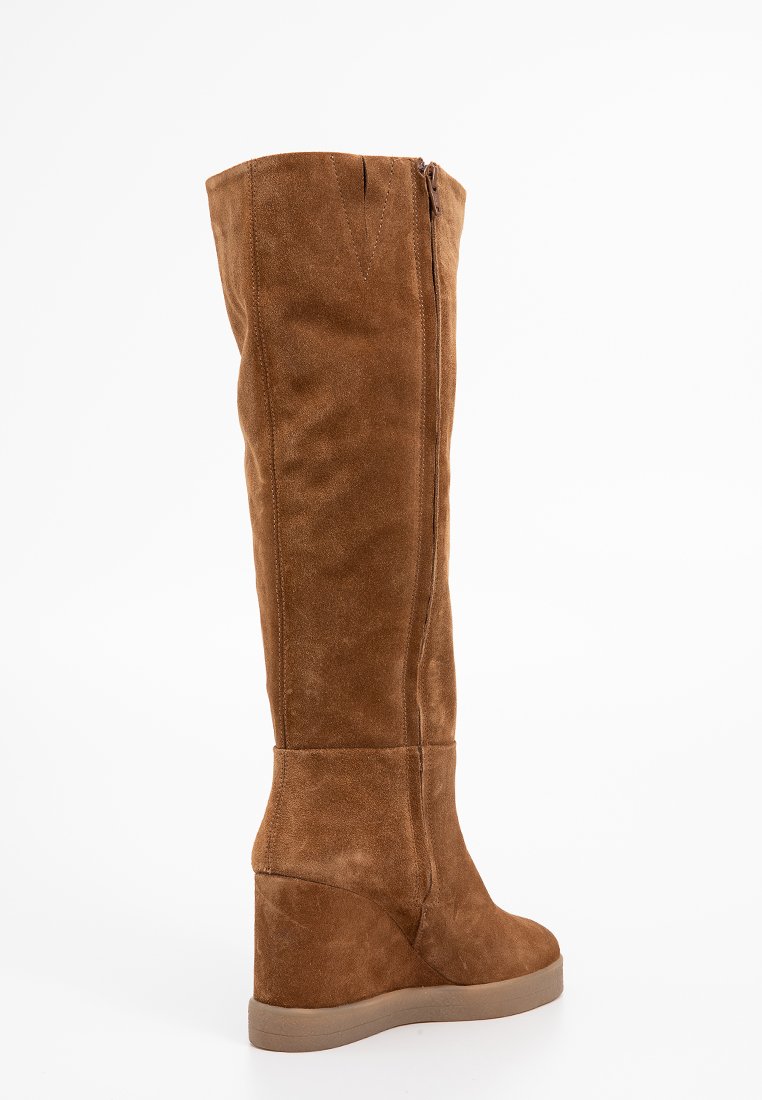 Bottes en daim marron au-dessus du genou avec un talon compensé, une fermeture éclair sur le côté, une texture lisse et un minimum de détails de couture.