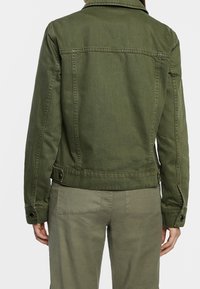 Olivgrüne Jeansjacke mit klassischem Kragen, seitlichen Taschen und verstellbaren knöpfbaren Manschetten. Hat ein sauberes Rückendesign mit minimaler Stitching.