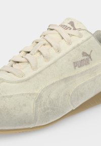 Baskets Puma beige clair avec laçage à l'avant, texture douce en cuir suédé et logo sur le côté et la languette, vues en gros plan sous un angle.