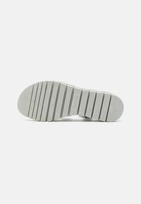 Suola di sneaker bianca in gomma con scanalature orizzontali e texture antiscivolo. Presenta una piccola stampa del logo e molteplici scanalature per una migliore aderenza.