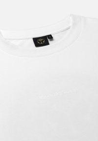 Weißes Baumwoll-T-Shirt mit Rundhalsausschnitt, das auf der Vorderseite mit dem eingeprägten Text "TOMORROWLAND" und auf der Rückseite mit einem schwarzen Etikett mit Logo versehen ist.