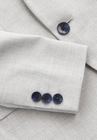 Veste de costume gris clair avec un revers comportant trois boutons bleu foncé et un bouton assorti près du col.