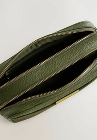 Groene leren tas met een gestructureerde afwerking, voorzien van gouden ritsen en meerdere compartimenten. Een open uitzicht toont de binnenvoering.