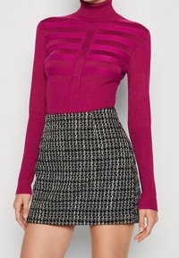 Un pull ras du cou fuchsia en maille avec des découpes horizontales associé à une mini-jupe en tweed texturé noir et blanc.