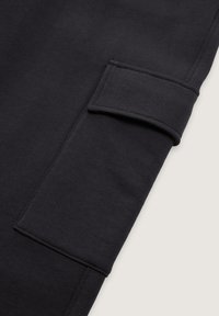 De zwarte sweatshirtstof heeft een omgeslagen manchet met een gestructureerde afwerking en zichtbare stiksel-details, wat een modern, minimalistisch ontwerp tentoonstelt.