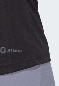 Juodas sportinis marškinėlis su AEROREADY logotipu, pagamintas iš tekstūruotos medžiagos su lygiomis siūlėmis. Marškinėliai dera su šviesiai pilkais apačia.