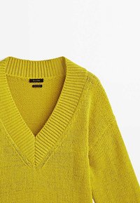 Pull en maille jaune-vert à col en V avec col côtelé et motif en tricot texturé, étiquette "Fabriqué en Turquie".