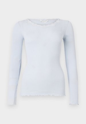Maglietta azzurra chiara a maniche lunghe realizzata in tessuto a coste con scollo in pizzo ondulato. Presenta un orlo asimmetrico e una silhouette aderente.