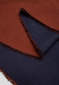Couverture en laine présentant un côté texturé orange brûlé et un côté bleu marine lisse avec des bords frangés, mettant en avant un design réversible.