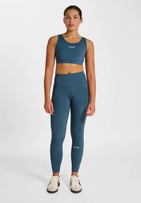 Blå sportig crop top och högmidjade leggings, båda med en slät textur och logodetaljer, kombinerade med avslappnade sneakers.