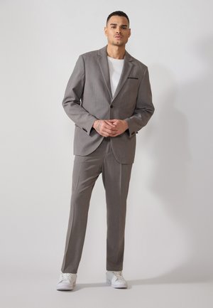 Traje gris a medida con un blazer de un solo botón y pantalones de frente plano. Llevado sobre una camisa blanca, combinado con zapatillas blancas.