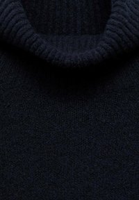 Primo piano di un maglione a collo alto lavorato a maglia nera che mostra la sua spessa struttura in tessuto a coste e il colletto ripiegato.