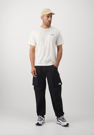 Hvid kortærmet t-shirt med et grønt logo, sorte cargo bukser med lommer og en beige kasket. Skoene er i sort og hvid athletic stil.