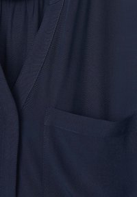 Marineblauwe stoffen overhemd met een V-hals, korte mouwen en een enkele borstzak met zichtbare stikseldetails. Glad textuur.