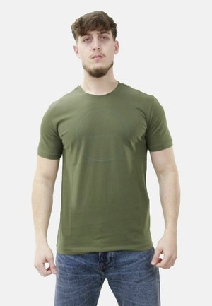 T-shirt a maniche corte color verde oliva realizzato in tessuto morbido, con un design grafico circolare in una tonalità più scura, abbinato a jeans blu.