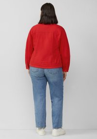 Rote Jeansjacke mit langen Ärmeln, Knopfmanschetten und einer verkürzten Passform. Getragen über hellblauen, geraden Jeans und weißen Sneakers.