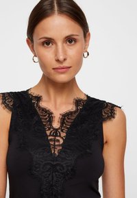 Μαύρη αμάνικη μπλούζα με βαθύ V λαιμόκοψη και περίπλοκες δαντελένιες λεπτομέρειες στον λαιμό και στους ώμους. Λείος υφασμάτινος υφή.