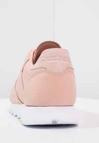 Ljust rosa sneaker med en slät läderöverdel och en mjuk mockahälflik, med minimal logotyp och en vit gummisula.