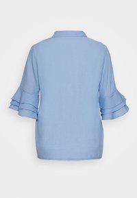 Ljusblå blus med knappstängning bak, krage och trekvartslånga volangärmar. Tillverkad av ett lätt, strukturerat tyg.