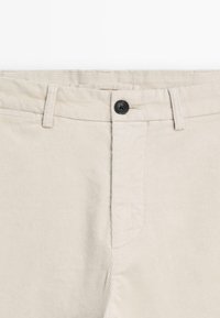 Beige corduroy pants with a straight-cut design, featuring a black button closure, belt loops, and vertical ribbed texture.
