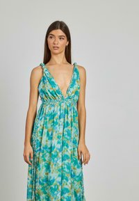 Maxi sukienka w niebiesko-zielony wzór tie-dye, z głębokim dekoltem w serek, plecionymi ramiączkami oraz przepływającym materiałem o luźnym kroju.