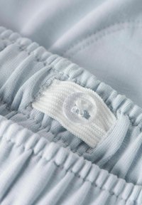 Indumento in tessuto blu chiaro con vita elasticizzata arr gatherata, caratterizzato da una sezione lavorata a maglia bianca e un dettaglio in plastica trasparente per la chiusura.