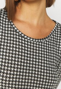 Černobílá tkanina s vzorem houndstooth a hladkým povrchem. Má kulatý výstřih a jemný pletený design.
