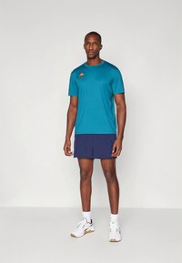 Meeste sportlik komplekt, mis koosneb sinisest lühikese varrukaga särgist ja tumedas sinises toonis lühikestest pükstest, valmistatud kergest kangast. Rinnal väike logo.