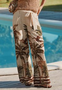 Pantalons larges légers en crème avec des imprimés de palmiers et de léopards, dotés de détails découpés et d'une taille nouée pour un ajustement personnalisé.