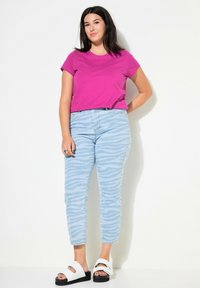 Růžová tričko s ozdobami, světle modré džíny se zebrovaným vzorem a bílé sandály s černou podrážkou.