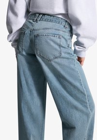 Jeanși din denim de culoare albastră deschisă, cu talie înaltă și croială relaxată. Prezintă două buzunare la spate și cusături vizibile. Textură moale, ușor decolorată.