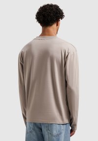 Beige shirt met lange mouwen van zachte stof, voorzien van een ronde hals en een ontspannen pasvorm, gecombineerd met lichtblauwe spijkerbroek.