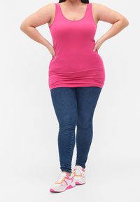 Fuchsia linne med rundad halsringning, matchad med blå skinny jeans och vita sneakers med rosa accenter och flerfärgade ränder.