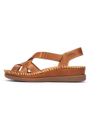 Brown leather sandal with crisscross design, woven accents, adjustable strap, and a cushioned outsole, featuring a rounded toe and low heel.
