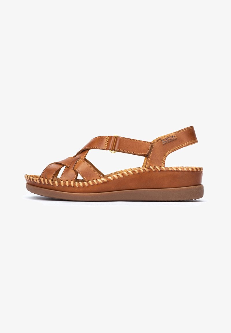 Brown leather sandal with crisscross design, woven accents, adjustable strap, and a cushioned outsole, featuring a rounded toe and low heel.