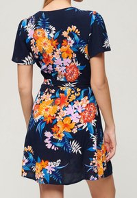 Blommig klänning med marinblå bakgrund, prydd med livliga orange, rosa och blå blommor, korta ärmar och ett figurnära midjeband.