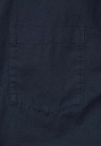 Telas azul marino con una textura suave presenta un único bolsillo trasero con una solapa triangular y costuras a juego.