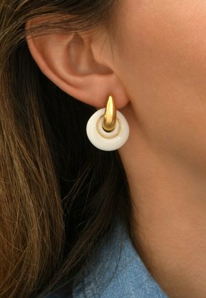 Boucles d'oreilles en ton or avec une base circulaire blanche, ornées d'un accent de perles autour du bord pour plus de détail et de texture.