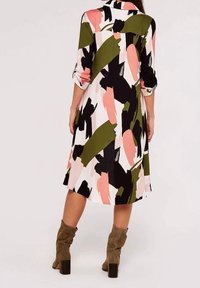 Vzorované šaty s kombinací růžových, zelených, černých a bílých tahů štětcem. Dlouhé rukávy, límec a délka ke kolenům s volným střihem.