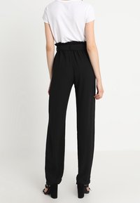 Pantalons noirs taille haute en tissu texturé, avec des jambes fuselées et une taille ceinturée. Associés à un haut blanc à manches courtes et des talons noirs.