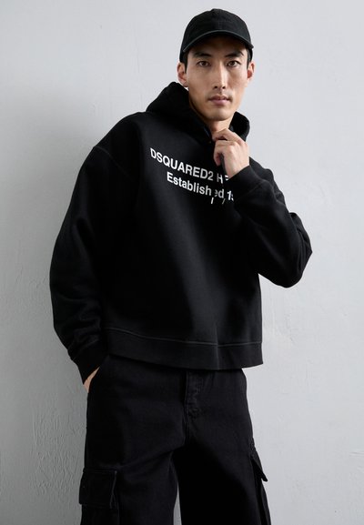 Schwarze verkürzte Kapuzenjacke mit dem weißen Drucktext "DSQUARED2 HW Established" und schwarzen Cargo-Hosen. Schlichtes Design, nicht strukturierter Stoff, lässiger Stil.
