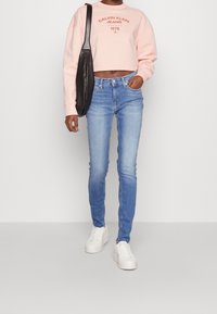 Sudadera recortada de color rosa claro con la impresión "CALVIN KLEIN JEANS", combinada con jeans ajustados azules y zapatillas de plataforma blancas. Incluido un bolso negro de hombro.