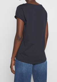 Camiseta de algodón azul marino con mangas enrolladas y un ajuste holgado, con escote redondo y dobladillo curvado. Combinada con pantalones de mezclilla de lavado claro.