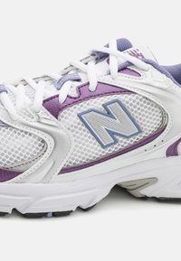 Białe i fioletowe buty sportowe z siateczkowymi panelami, grubymi podeszwami i wyraźnym logo "N" po boku.