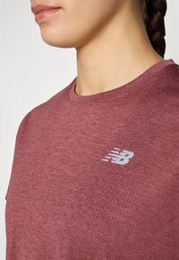 T-shirt de sport bordeaux en tissu texturé, avec un logo gris subtil sur le côté gauche et un design classique à col rond.