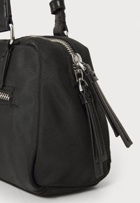 Μαύρη τσάντα χειρός από ύφασμα με υφή, διαθέτει ασημένιο μεταλλικό φερμουάρ και δερμάτινες λεπτομέρειες. Συμπαγής σχήμα με αποσπώμενο λουρί.