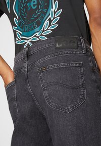 Schwarze Jeans aus Denim verfügen über eine Gesäßtasche mit einem kleinen Logotag und einen strukturierten Taillenbund. Der Stoff ist leicht ausgewaschen, was das Design hervorhebt.