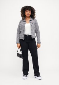 Chaqueta de mezclilla gris con cierre de botones, camiseta sin mangas blanca, pantalones de pierna ancha negros y bolso negro. Zapatillas blancas con acentos negros.