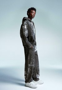 Dark denim tracksuit with a textured black and white pattern, featuring a hooded jacket and straight-leg pants. White sneakers complete the look.