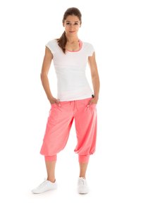 Weißes, enges T-Shirt mit pinkem Saum; lockere, pinke Jogginghosen bis zur Mitte der Wade mit elastischem Bund; kombiniert mit weißen Sportschuhen.